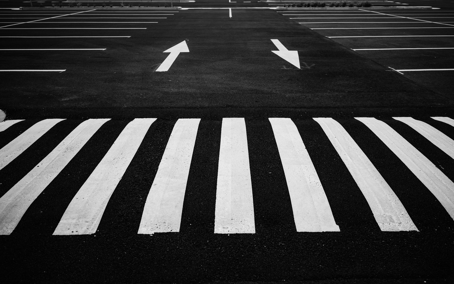 Black and white image of a parking lot with zebra crossing and directional arrows.